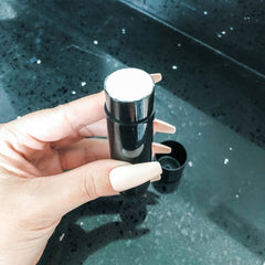 Black cylindrical container with white product and black cap, held in hand