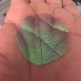 Eye shadow swatch with green and purple multichrome color, textured pattern, on hand