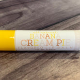 Lip balm tube with yellow and white, banana cream pie text, on wood surface