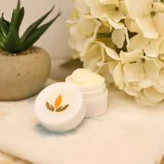 White cream jar with open lid, white container with orange logo, on a white surface