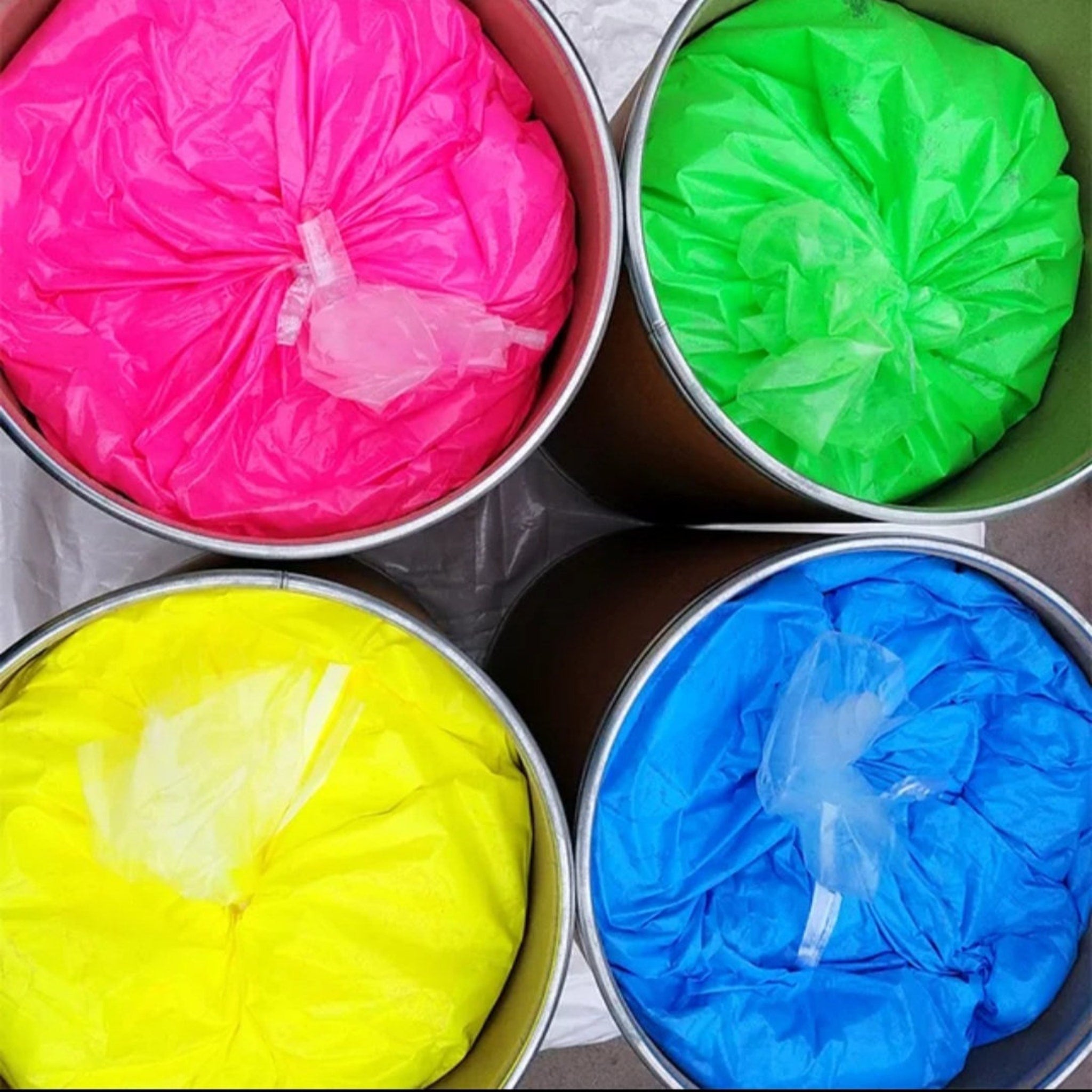 Eye shadow powders in pink, green, yellow, and blue plastic bags inside metal containers