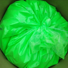 Green plastic bag, crumpled material, tied with string, inside a box.