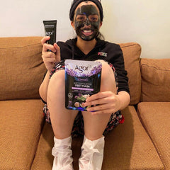 Feet mask with Agor branding, black face mask, and white foot coverings on person sitting on couch