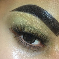 Eye makeup with green and gold glitter eyeshadow, black eyebrow, and dark eyelashes