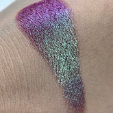 Eye makeup swatch with purple and teal sparkle, applied on skin