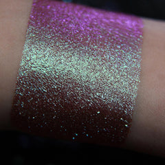 Glitter eyeshadow swatch with purple and teal shimmer on skin, showing color and texture