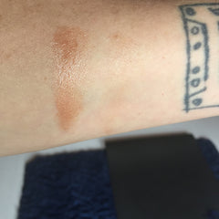 Bronzer swatch, brown and shimmering, applied on skin, with tattoo visible