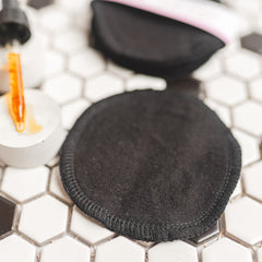 Reusable black cotton pads with stitched edges on hexagonal tile surface