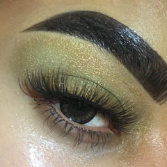 Eye makeup featuring green and gold eyeshadow with long black eyelashes and a dark eyebrow.