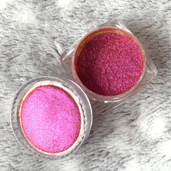Pink glitter eyeshadow in clear plastic jars on a textured white surface