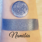 Shimmer eyeshadow swatch in blue-gray with metallic finish, applied on skin, "Namibia" text