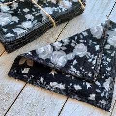 Reusable cloth pads, black floral pattern with gray roses, stacked on wood surface