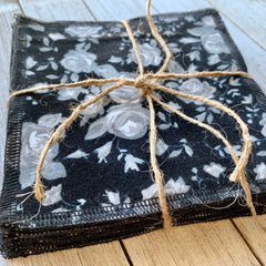 Cloth napkins with black floral pattern, tied with twine, stacked on wood surface