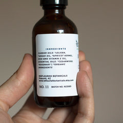 Brown glass bottle with white label, held in hand, Re|flourish Botanicals label visible