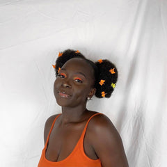 Woman with orange top and floral hair accessories, against white background