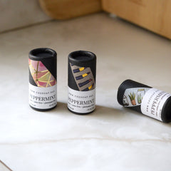 Lip balm tubes with black paper, patterned labels, and white text on a white surface
