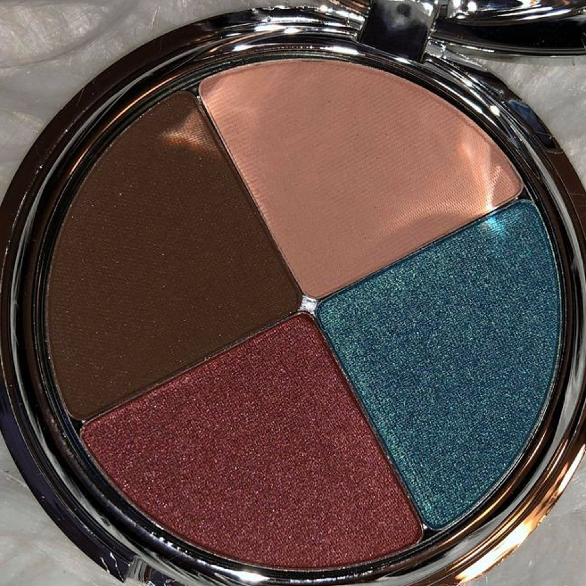 Eye shadow palette with brown, pink, teal and red shades in a silver compact