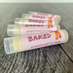 Lip balm tubes with pink labels, gingerbread illustration, and "BAKED" text on wood surface