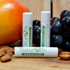 Lip balm tubes with white and green labels, next to fruit and nuts on wood surface.