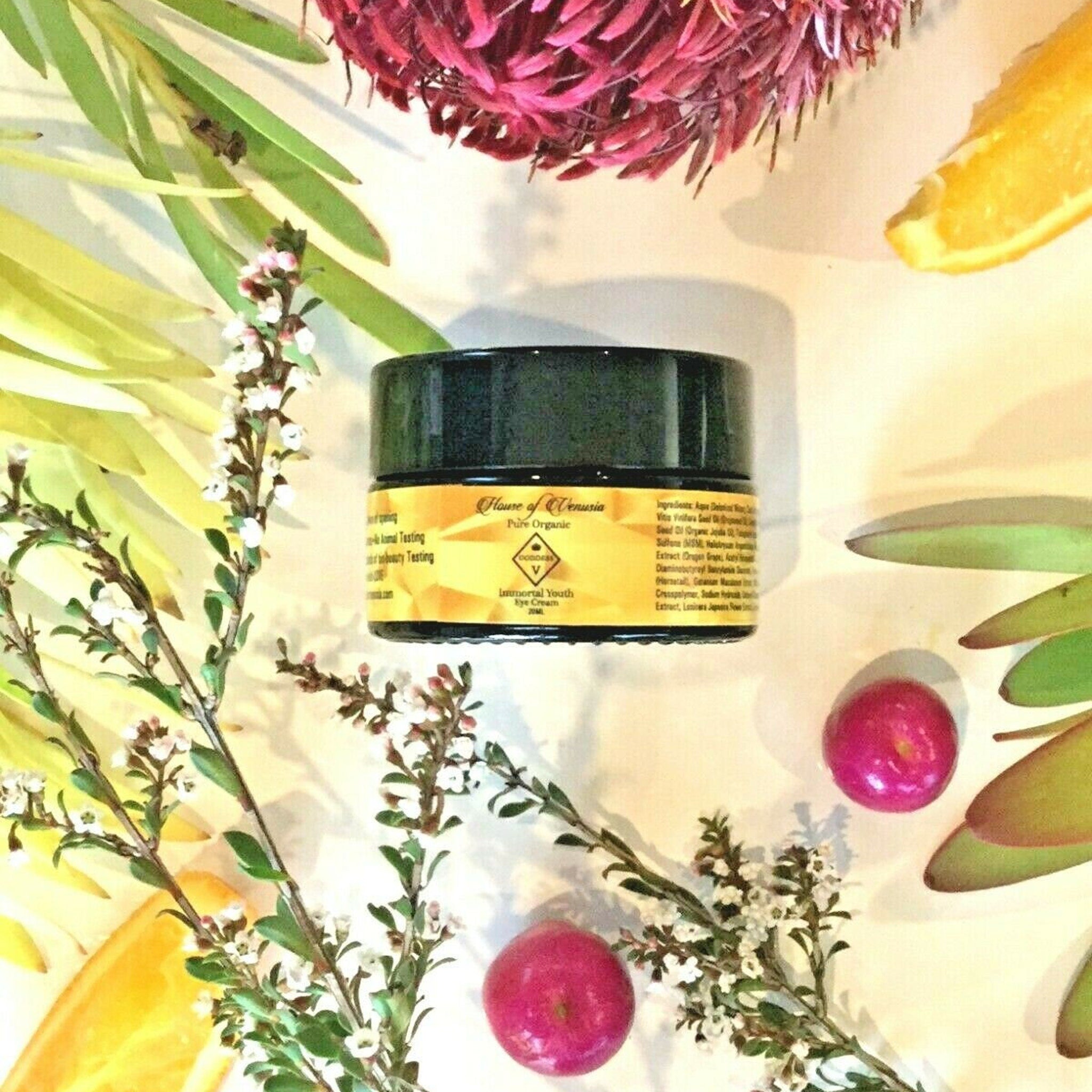 Eye cream jar with black lid, yellow label, and botanical arrangement with House of Venusia text