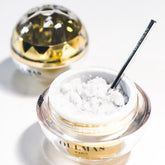 Facial cleanser with white crystals, glass jar, gold rim, and silver spoon in use