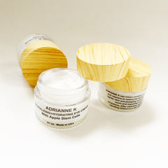 Eye cream jars with white cream, glass and wood lids, ADRIANNE K text visible