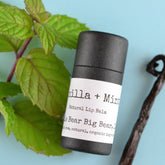 Lip balm tube with black paper, white label, and green mint leaves on blue background