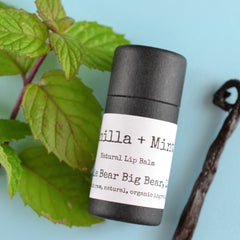 Lip balm tube with black paper, white label, and green mint leaves on blue background