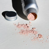 Facial cleanser powder, pink powder spilled, silver metal container, cap off