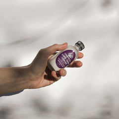 Facial exfoliant bottle, white and purple label, held in hand, Visions Co brand visible