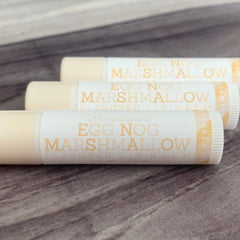 Lip balm tubes with white and orange labels, Egg Nog Marshmallow text, and cream colored tubes