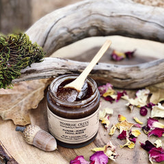 Facial scrub jar with dark brown contents, wooden spoon, and Moonrise Creek label on wood surface