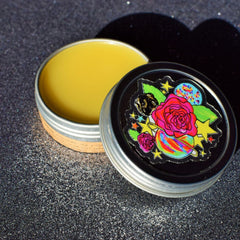 Lip balm in silver tin with yellow balm, black lid with colorful floral design, open