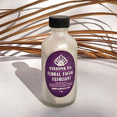 Floral facial exfoliant bottle with purple label, black cap, and Visions Co. text