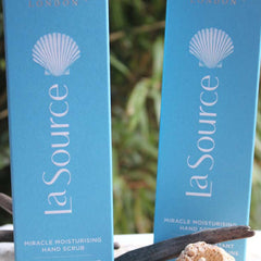 Hand scrub bottles, light blue with white seashell logo, "La Source" text visible