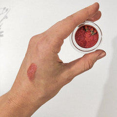 Red eyeshadow with shimmer, applied to skin, held in clear container