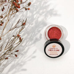 Eyeshadow shimmer with red-orange color, clear jar, black lid with "TWIN FLAME" text, VISIONS Co brand