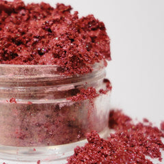 Red glitter eyeshadow in a clear plastic container with scattered particles on white background