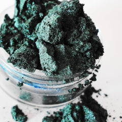 Green eyeshadow powder with glittery texture in a clear container on white background