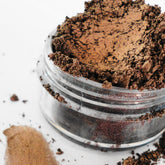 Eye shadow with pale brown and gold shimmer in a clear jar on white background