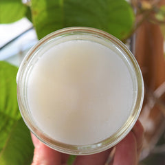 Sugar scrub in clear glass jar with off-white contents, held by hand, overhead view