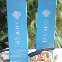 Hand scrub product with blue packaging, white seashell logo, and Crabtree & Evelyn brand text visible