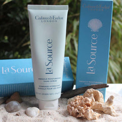 Hand scrub tube in light blue with white cap, Crabtree & Evelyn brand on sand with coral