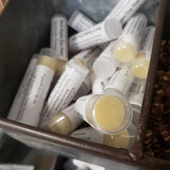 Lip balm tubes with white labels, yellow balm, and clear caps in a metal container.