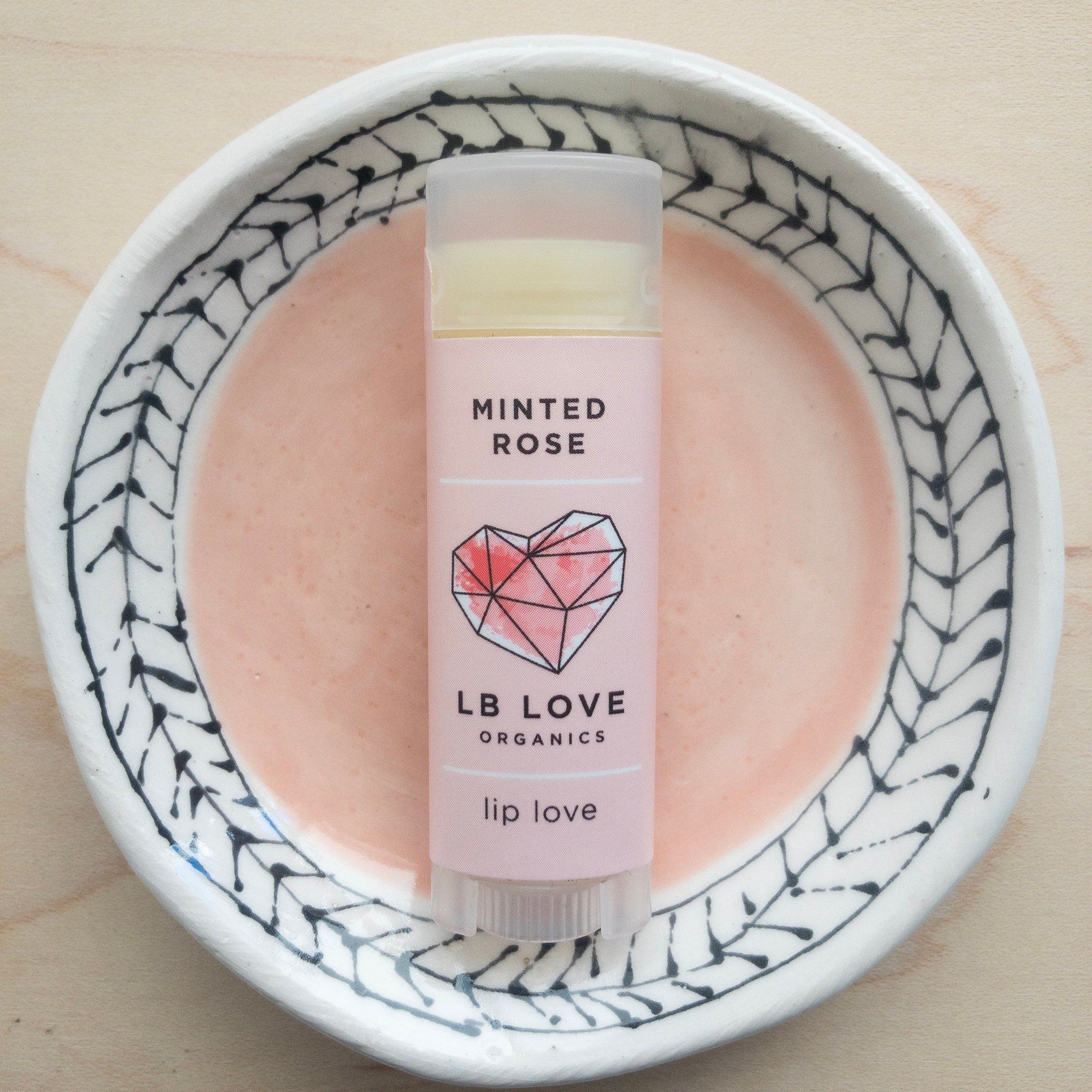 Lip balm tube with pink label, clear cap, and LB Love text on a decorative plate
