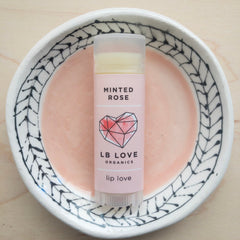 Lip balm tube with pink label, clear cap, and LB Love text on a decorative plate