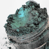 Eyeshadow shimmer, teal green metallic powder in clear jar, close-up view