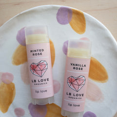 Lip balm tubes with pink labels, clear caps, and LB Love branding on a decorative plate