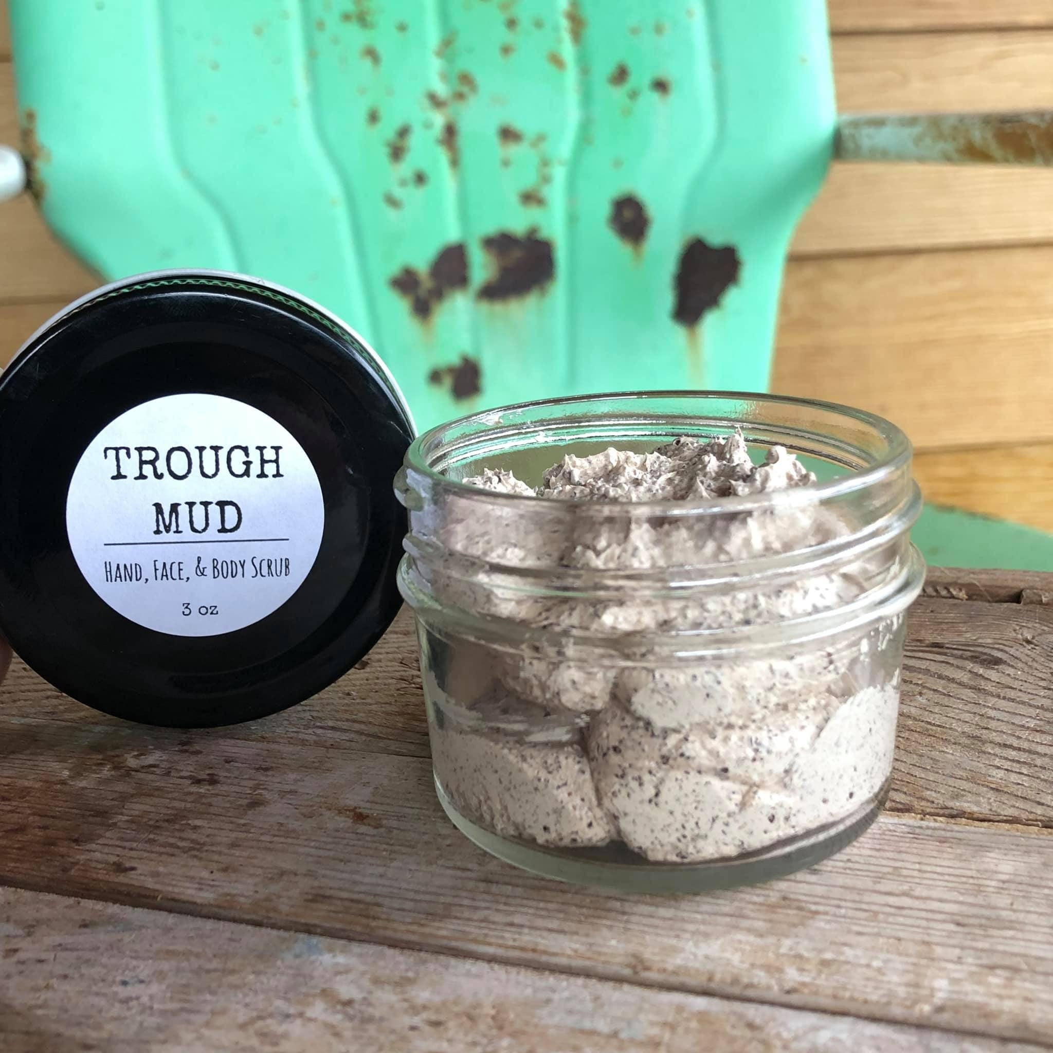 Exfoliation scrub in glass jar with speckled cream color, next to black jar lid with text "TROUGH MUD