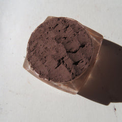 Brown powder compact with textured surface and clear glass container, top view